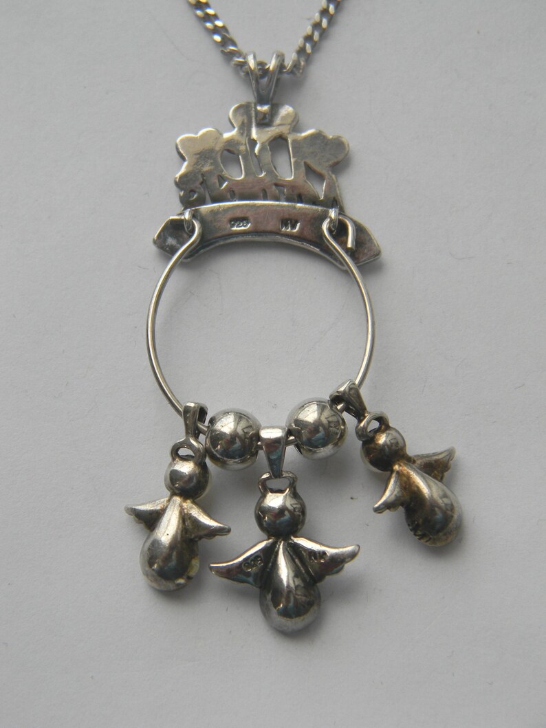 Op de afbeelding: Zilveren hanger ketting met een cirkelvormig ontwerp en drie kleine engel bedels die eronder hangen. De hanger heeft een decoratieve bovenkant met een kroonachtig ontwerp en is opgehangen aan een delicate ketting.