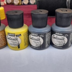 May include: Six small bottles of fabric dye, labelled "Setasilk" in a variety of colours, including brown, yellow, grey, and blue.