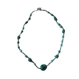 May include: A turquoise and silver necklace with a large turquoise pendant. The necklace is made of small turquoise beads and silver beads.