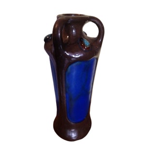 May include: A brown ceramic vase with blue glaze and decorative accents. The vase has two handles and a unique, organic shape.