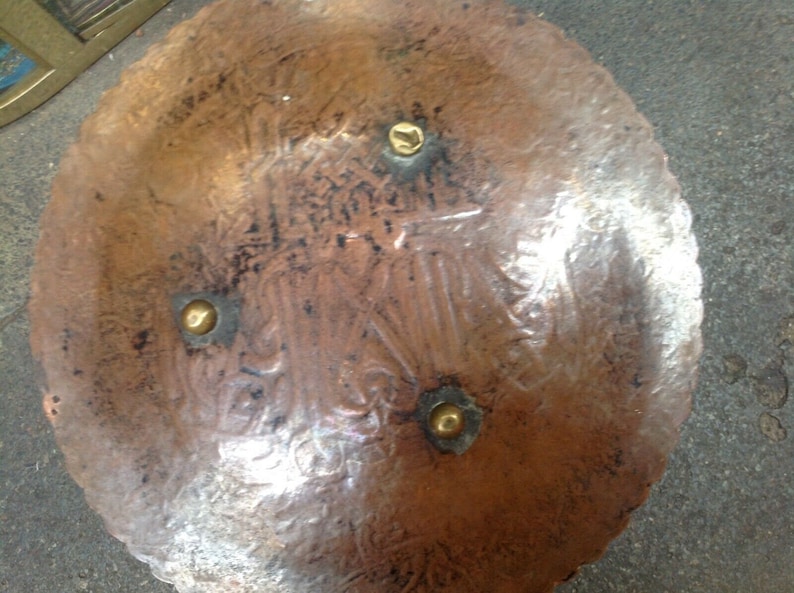 May include: A copper plate with a decorative design and four brass accents. The plate is round and has a scalloped edge.