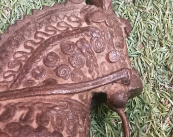 Könnte beinhalten: Eine detailreiche, verzierte, braune Metallpferdeskulptur mit komplizierten Designs. Der Kopf des Pferdes ist zur Seite gedreht, und die Skulptur ist vor einem grünen Hintergrund platziert.