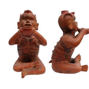 Könnte beinhalten: Zwei Terrakotta-Figuren einer sitzenden Figur mit einer Tasse in den Händen. Die Figuren sitzen mit erhobenen Händen zum Mund, als würden sie aus der Tasse trinken. Die Figuren sind aus rotbraunem Ton gefertigt und haben ein rustikales, handgemachtes Aussehen.