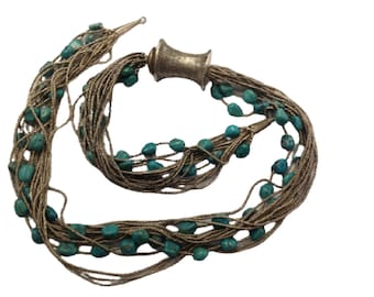 May include: A multi-strand necklace featuring strands of metallic beads and turquoise-colored stones. The necklace has a silver-toned clasp and is displayed against a white background. The necklace is a jewelry item.