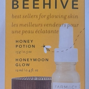 Może przedstawiać: Żółte pudełko z wzorem ula i tekstem "FARMACY THE BEEHIVE" z przodu. Pudełko zawiera dwa produkty do pielęgnacji skóry: Honey Potion, nawilżającą maskę o pojemności 15 gramów, oraz Honeymoon Glow, serum do twarzy z AHA o pojemności 12 ml. Pudełko zawiera również próbkę Green Clean.