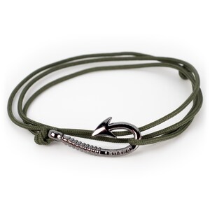 Puede incluir: Un brazalete de cordón verde con un cierre de gancho plateado.