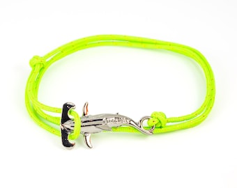 Könnte beinhalten: Ein neongrünes Armband mit einem silberfarbenen Hammerhai-Anhänger. Das Armband besteht aus einem gewebten Kordel und hat einen Knotenverschluss. Der Hai-Anhänger hat detaillierte Merkmale und einen Hakenverschluss.