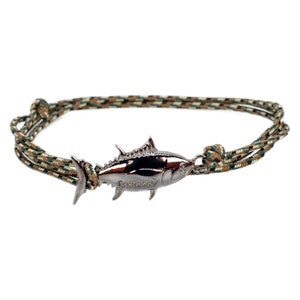 May include: A green, brown, and white braided rope bracelet with a silver tuna fish charm. The charm has the word "Castaway" engraved on it.