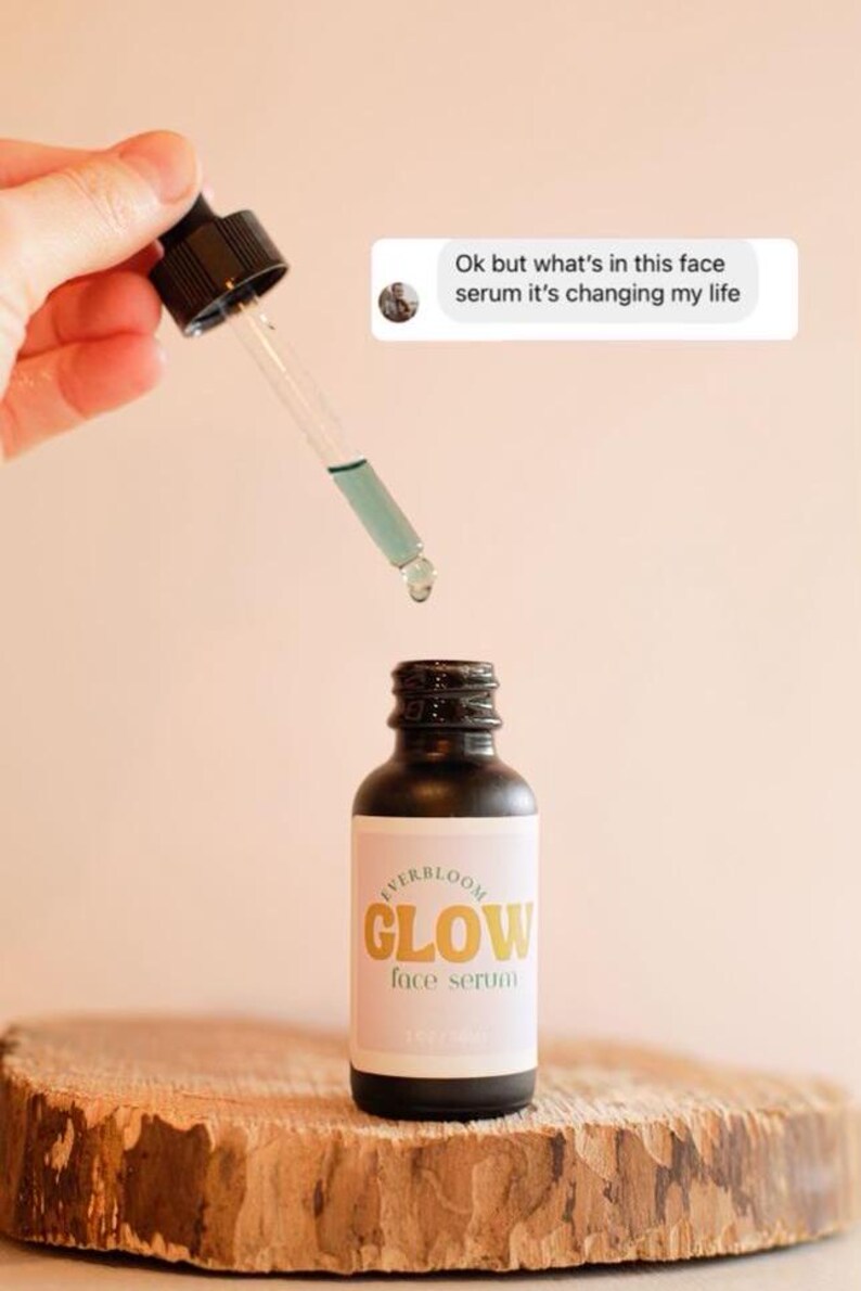 Puede incluir: Una botella de vidrio con un gotero negro y una etiqueta que dice "EVERBLOOM GLOW face serum". La botella est&aacute; sobre una superficie de madera. El gotero est&aacute; lleno de un l&iacute;quido azul claro.