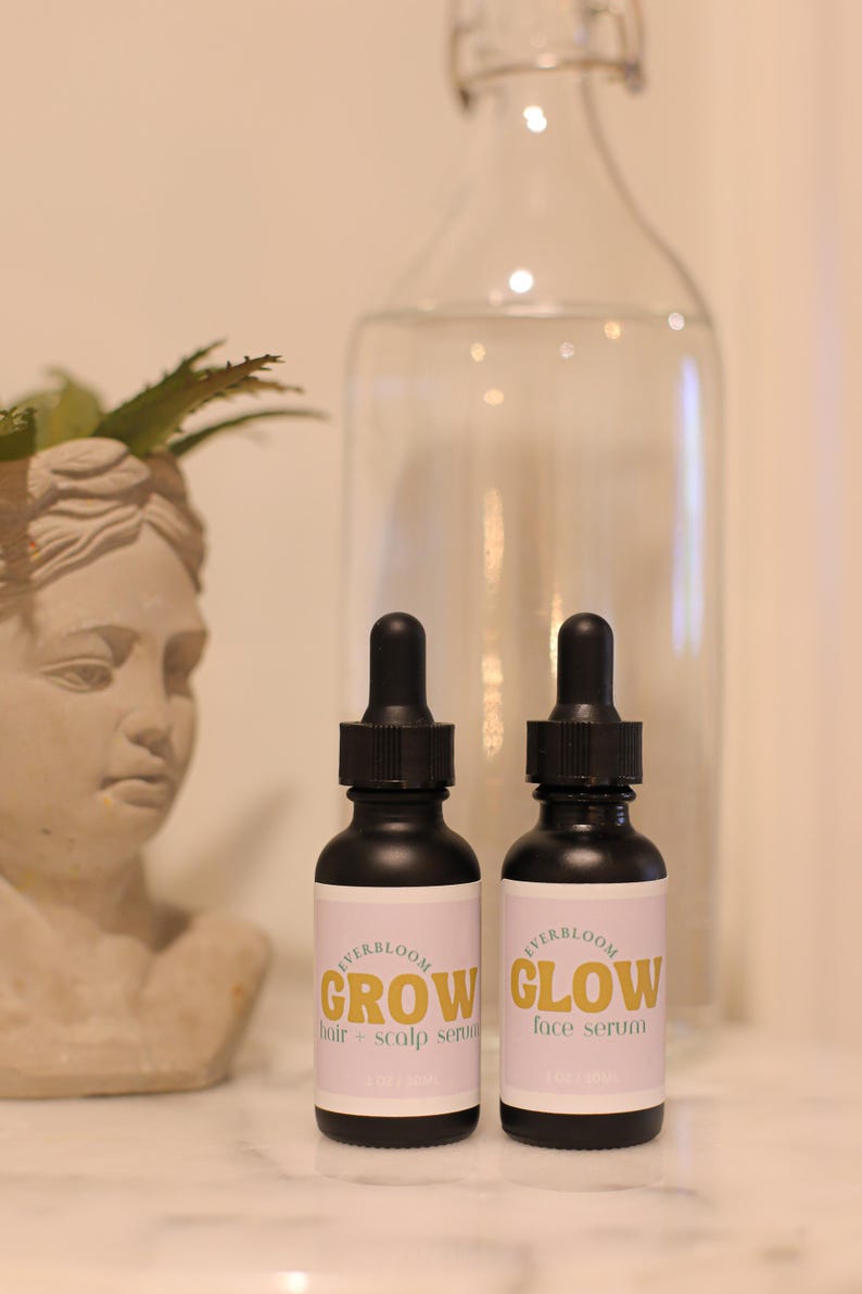 Puede incluir: Dos peque&ntilde;os frascos negros con goteros. Los frascos est&aacute;n etiquetados con "EVERBLOOM GROW suero para cabello y cuero cabelludo" y "EVERBLOOM GLOW suero facial".