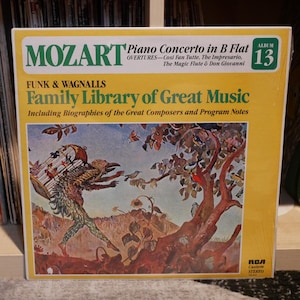 Może przedstawiać: Żółta okładka winylowego albumu z kolorową ilustracją ptaka niosącego klatkę. Album nosi tytuł "Mozart Family Library of Great Music" i zawiera tekst "Piano Concerto in B Flat" oraz "Album 13".