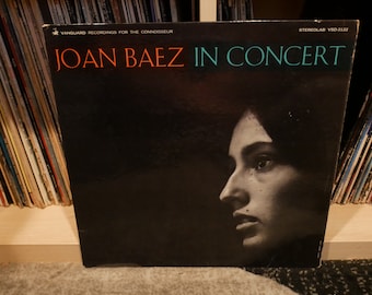 May include: A black vinyl record album cover with the text "Joan Baez In Concert" in orange and teal lettering. The cover features a black and white photo of Joan Baez's face.