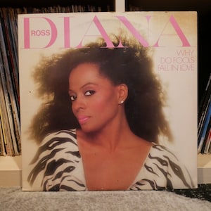 Puede incluir: Una portada de álbum de vinilo con Diana Ross. La portada es blanca con texto rosa que dice "Diana Ross" y "Why Do Fools Fall In Love". La portada del álbum presenta una foto de Diana Ross con un top de estampado de cebra y mirando directamente a la cámara.