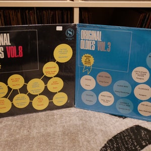 Op de afbeelding: Twee vinyl platen, een blauwe en een zwarte, met de titel "Original Oldies" en een volumenummer. De platen hebben een cirkelvormig ontwerp met songtitels en artiestennamen.