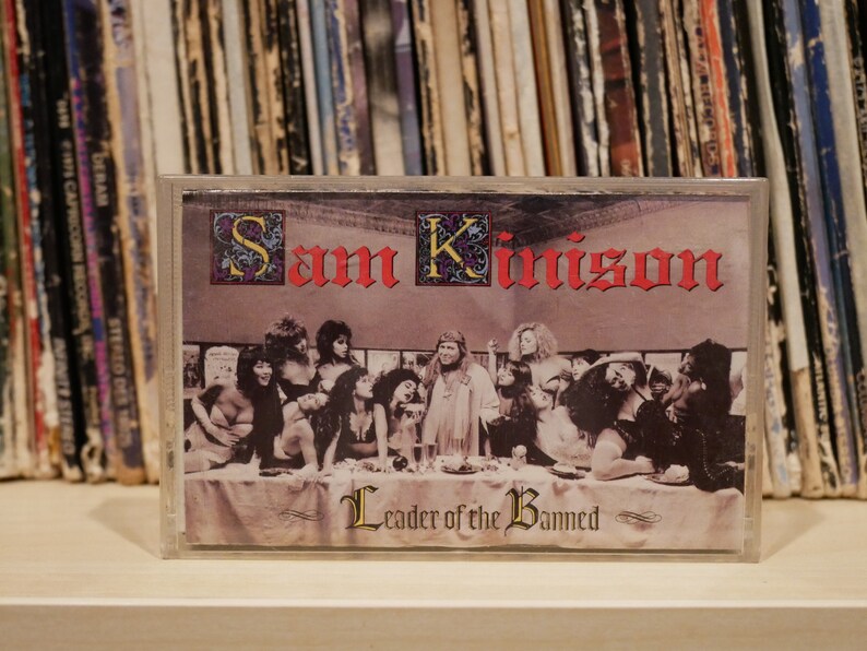 May include: A cassette tape with the album art for "Sam Kinison: Leader of the Banned." The artwork is a parody of The Last Supper, with Kinison as the central figure. The title and artist's name are in red gothic lettering.