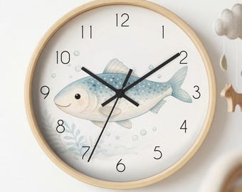 May include: A round wall clock with a light wood frame and a white face. The clock features black numbers from 1 to 12 and black hands. A watercolour illustration of a blue fish with white spots is centred on the face, surrounded by bubbles.