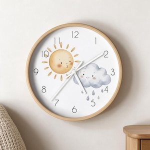 May include: A round wall clock with a light wood frame and a white face. The dial features black numerals and a whimsical illustration of a smiling sun and a rain cloud with droplets. Three thin white hands indicate the time on the clock face.