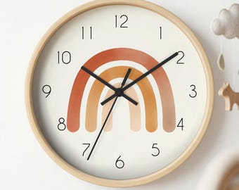 May include: A round wall clock with a light wood frame and a cream-coloured face. The centre features a multi-coloured rainbow graphic in shades of terracotta, orange, and beige. It has black hour, minute, and second hands and black numerals.
