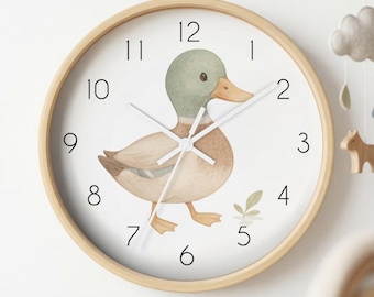 May include: A round wall clock with a light wood frame and a white face. The clock features a watercolour illustration of a brown duck with a green head, black numerals from 1 to 12, and three thin white clock hands indicating the current time.
