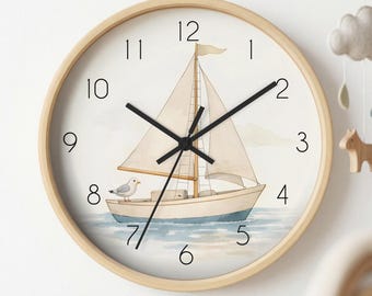 May include: A round wall clock with a light wood frame and a white face featuring a watercolour illustration of a sailboat on blue water with a small seagull on the deck. The clock has black hour, minute, and second hands and black numerals.