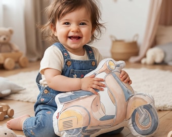 May include: A plush throw cushion shaped like a vintage scooter in soft pastel peach and blue tones. The cushion features a detailed illustration of a scooter with a round headlight, a seat, and wheels, designed with a smooth fabric finish.