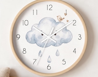 May include: A round wall clock with a light wood frame and a white face. The center features a watercolor illustration of a blue cloud with a face, a small bird, and two hearts. Three blue raindrops fall below the cloud. Black numbers mark the hours.