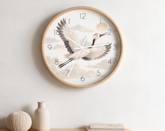 May include: A round wall clock with a light wood frame featuring a white face. The clock displays a watercolor illustration of a white crane in flight against a background of soft clouds and a pale sun. It has black numerals and white hands.