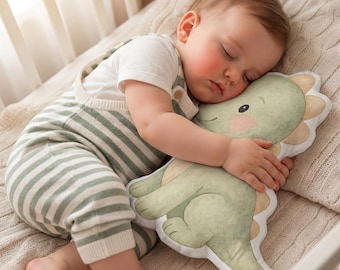 May include: A plush dinosaur-shaped cushion featuring a soft green and cream watercolour-style illustration of a friendly dinosaur with rounded features, a long tail, and a scalloped back crest, designed as a huggable stuffed toy for comfort.