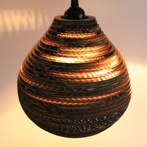 May include: A round, brown cardboard pendant light with a layered design. The light is lit and casts a warm glow.