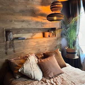May include: A cosy bedroom with a wooden wall, a bed with brown and white pillows, and a set of three hanging pendant lights with a woven design.