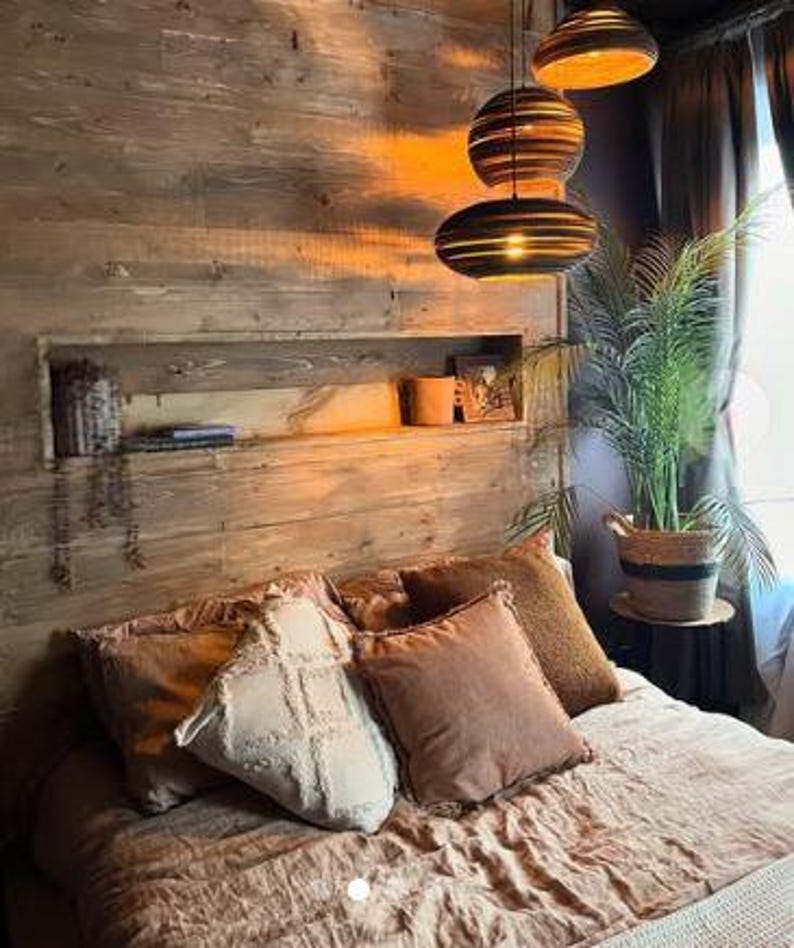 May include: A cosy bedroom with a wooden wall, a bed with brown and white pillows, and a set of three hanging pendant lights with a woven design.