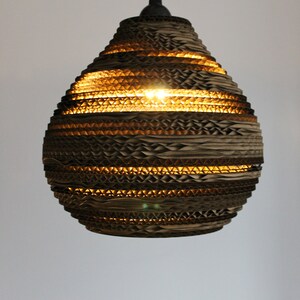 May include: A brown cardboard pendant light with a honeycomb pattern. The light is turned on and illuminates the room.