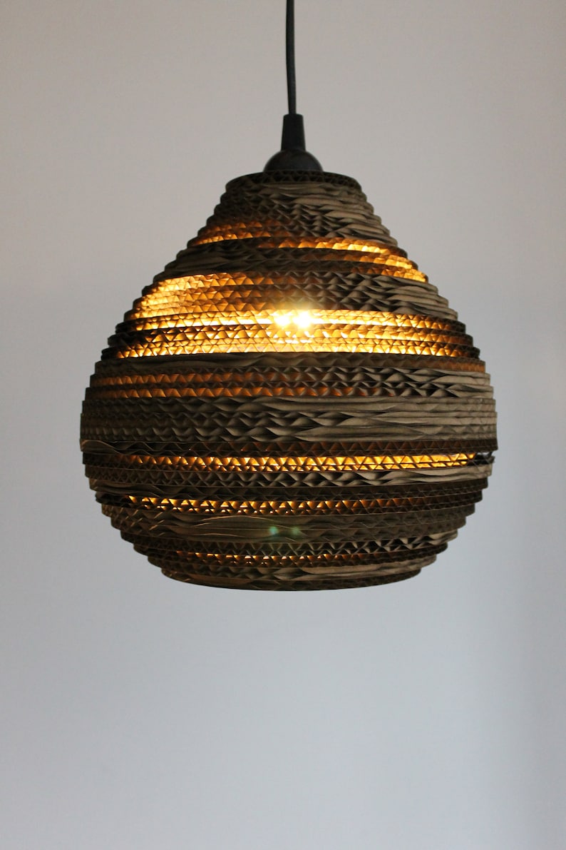 May include: A brown cardboard pendant light with a honeycomb pattern. The light is turned on and illuminates the room.