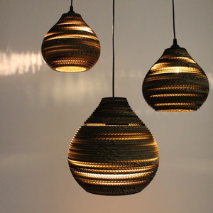 May include: Three hanging pendant lights made of brown cardboard with a layered, textured design. The lights are round and have a teardrop shape.