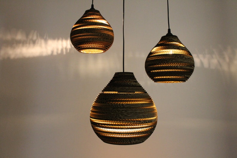 May include: Three hanging pendant lights made of brown cardboard with a layered, textured design. The lights are round and have a teardrop shape.