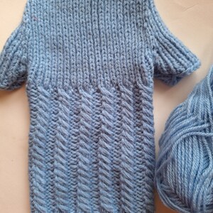 May include: A light blue knitted garment with a textured pattern. The garment has long sleeves and a ribbed hem. A ball of light blue yarn is also pictured.