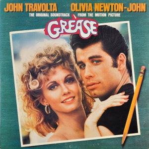 May include: Album cover for the Grease soundtrack featuring John Travolta and Olivia Newton-John. The title "Grease" is in a red and white stylized font. A yellow pencil with a pink eraser is in the lower right corner.
