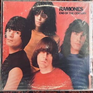 May include: Album cover for the Ramones' "End of the Century." The cover features four band members with long, dark hair and a red background. The band's name and album title are printed in white.