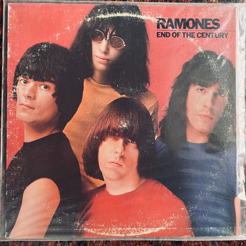 May include: Album cover for the Ramones' "End of the Century." The cover features four band members with long, dark hair and a red background. The band's name and album title are printed in white.