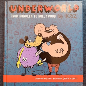 May include: A hardcover book titled "UNDERWORLD" with the subtitle "FROM HOBOKEN TO HOLLYWOOD by Kaz." The cover features cartoon illustrations of two characters and the text "FOREWORD BY PATRICK MCDONNELL. CREATOR OF MUTTS" at the bottom.