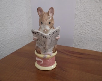 May include: A ceramic figurine of a mouse reading a newspaper titled "The Tailor & Cutter." The mouse is perched on a spool of thread. The figurine is painted in shades of brown, pink, and cream.