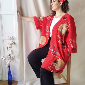 May include: A red kimono with a white and gold pattern of clouds and birds. The kimono is worn over a white t-shirt and black pants.