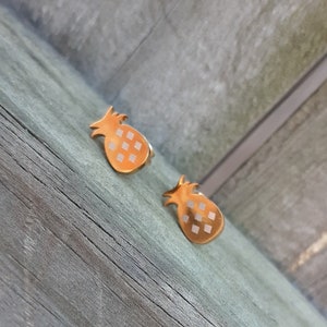 May include: A pair of gold pineapple earrings with a white enamel design.