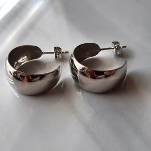 May include: A pair of silver hoop earrings with a smooth, rounded surface. The earrings are simple and elegant.