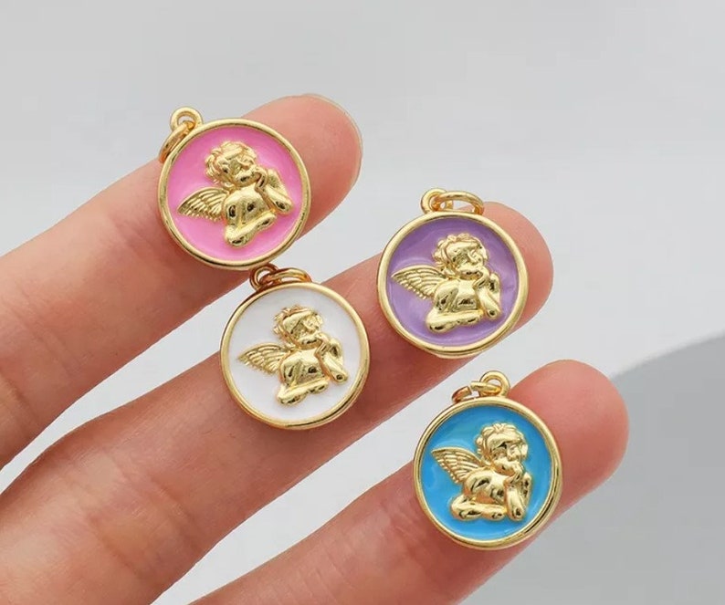 K&ouml;nnte beinhalten: Vier goldfarbene Engelscharms mit Emaille-Akzenten. Die Charms sind rund und zeigen einen Cherub mit Fl&uuml;geln. Die Emaillefarben sind rosa, lila, wei&szlig; und blau.
