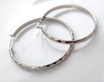 May include: A pair of silver hoop earrings with a textured finish. The earrings are large and have a simple, elegant design.