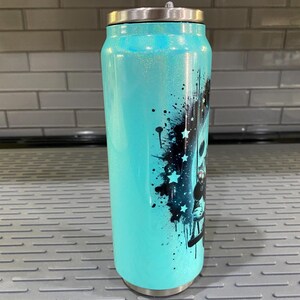 Puede incluir: Un vaso de purpurina turquesa con tapa plateada. El vaso presenta un dise&ntilde;o gr&aacute;fico negro con estrellas y salpicaduras de pintura. El vaso est&aacute; dise&ntilde;ado para parecerse a una lata de refresco.