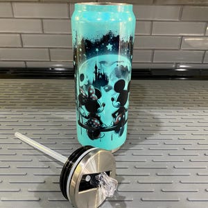 Puede incluir: Un vaso de color turquesa con tapa y pajita. El vaso presenta un dise&ntilde;o de Mickey y Minnie Mouse frente a una luna llena y un castillo. El vaso tiene un acabado brillante.