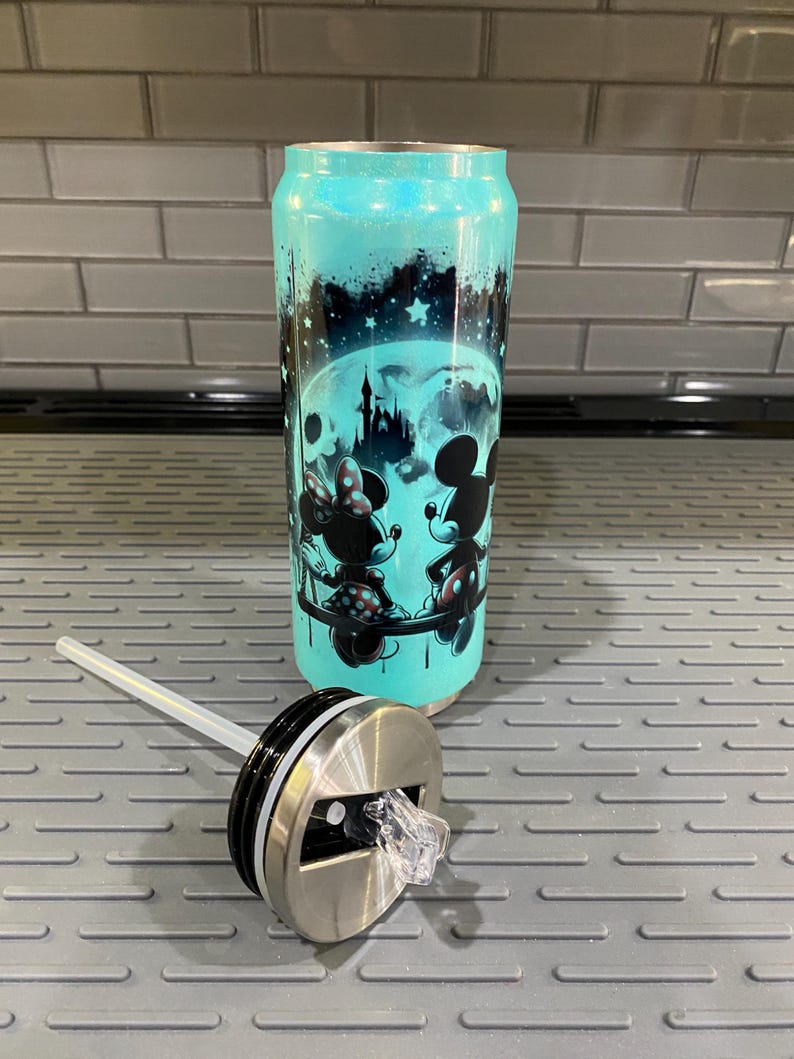 Puede incluir: Un vaso de color turquesa con tapa y pajita. El vaso presenta un dise&ntilde;o de Mickey y Minnie Mouse frente a una luna llena y un castillo. El vaso tiene un acabado brillante.