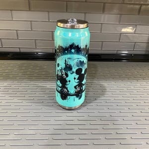 Puede incluir: Un vaso de acero inoxidable de color turquesa con tapa plateada y cierre abatible transparente. El vaso presenta una ilustraci&oacute;n en blanco y negro de Mickey y Minnie Mouse, con un castillo y un dise&ntilde;o de cielo estrellado.